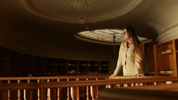 Atractiva joven rubia con gafas posando en la antigua biblioteca vintage sobre una cálida luz pálida — Vídeo de stock