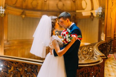 Muhteşem genç gelin ve lüks iç arka plan ile eski Ahşap korkuluk çubuğu yakınındaki yakışıklı zarif damat