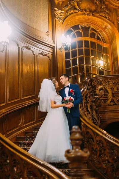 Charming bride and handsome elegant groom on old wooden stairs with the background of vintage interior — Stock Photo, Image