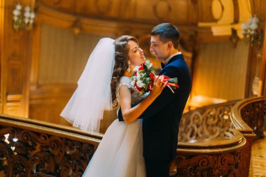 Büyüleyici gelin ve lüks iç arka plan ile eski Ahşap korkuluk çubuğu yakınındaki zarif yakışıklı damat