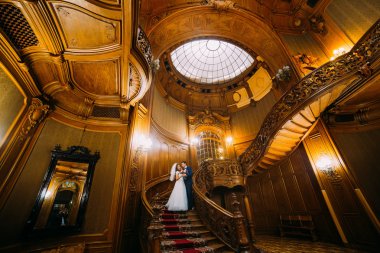 Sevimli gelin ve lüks iç arka plan ile eski ahşap merdivenlerde yakışıklı zarif damat