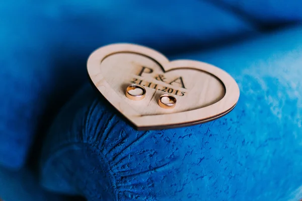 Dois anéis de casamento caros dourados em uma placa de madeira fantasia em uma almofada de sofá azul — Fotografia de Stock