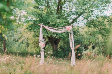 Ahşaptan yapılmış kemer beyaz pamuklu tekstil, pembe çiçek ve yeşillik, tören alanında ormanda ayakta dekore edilmiş.