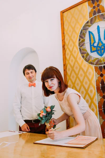 Bride signing marriage license or wedding contract and looking at camera, while groom standing behind — Stock Photo, Image