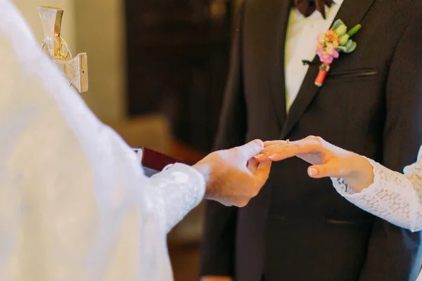 Sacerdote está poniendo el anillo en el dedo de las novias durante la ceremonia de boda — Foto de Stock