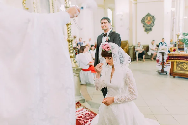 Mariée prie sur les genoux debout devant le prêtre dans l'église — Photo