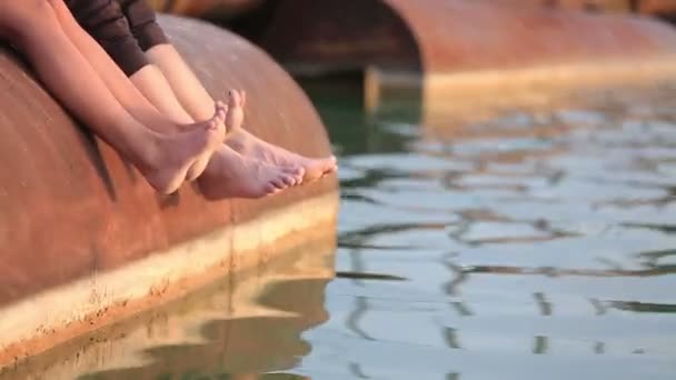 Romantikus pár pihentető a közeli tavon naplementekor. A fiatalok a csupasz lábak, a víz felszínén — Stock videók
