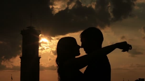 Silhueta de jovem casal amoroso suavemente beijando no telhado da cidade antiga edifício de perto. Pôr-do-sol romântico com torre velha no fundo — Vídeo de Stock