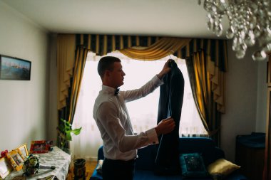 Otel odasında pencerenin önünde ceketini tutan zarif lüks delikanlı