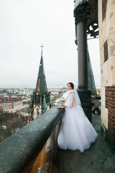 Elegante bruid poses op het balkon van de toren van de oude gotische kathedraal — Stockfoto