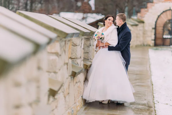 Casal recém-casado apaixonado romântico feliz abraçando juntos perto da parede do castelo velho — Fotografia de Stock