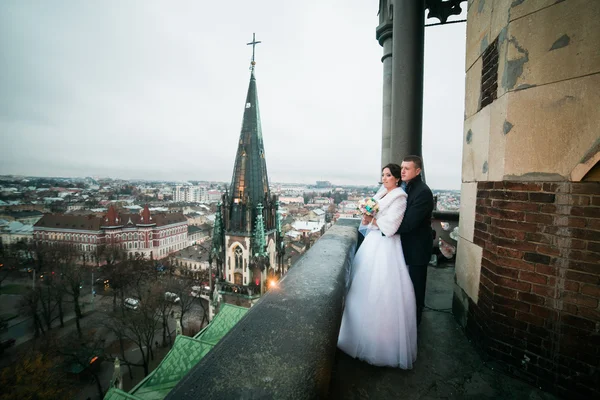 Happy bride and groom holding each other on the balcony of old gothic cathedral — Stock Photo, Image