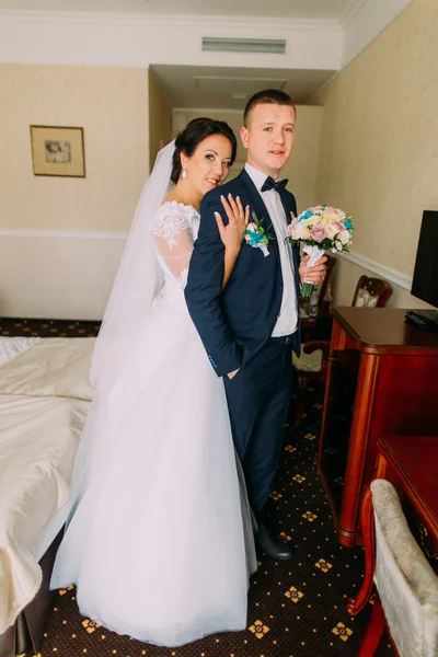 Splendida sposa ed elegante sposo in posa in camera d'albergo dopo la cerimonia nuziale. Ritratto di sposi in luna di miele — Foto Stock