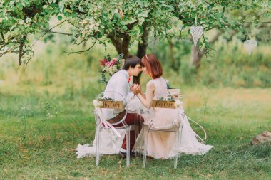 Gelin, ormanda oturan damat, arkadan görmek. Onun ve onun için işaretlerle süslenmiş iki şeffaf sandalye.