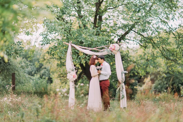 Feliz pareja romántica recién casada besándose en el pasillo de la boda con decoraciones rosas y flores —  Fotos de Stock