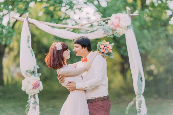 Schöner Bräutigam küsst schöne Rotkopfbraut während der Hochzeitszeremonie in der Nähe des Bogens — Stockfoto