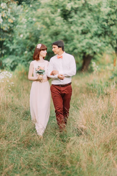 Gelukkig Newlywed bruid en bruidegom wandelen houden handen in het zomer bos. Vrouw met rood haar. — Stockfoto