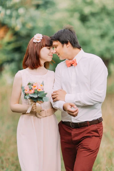 Schöne Braut mit rotem Haar und glücklichem Bräutigam, die zusammen auf dem Hintergrund des grünen Waldes spazieren gehen — Stockfoto