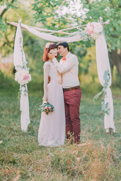 Красивий наречений цілує наречену під час весільної церемонії біля квіткової арки . — стокове фото