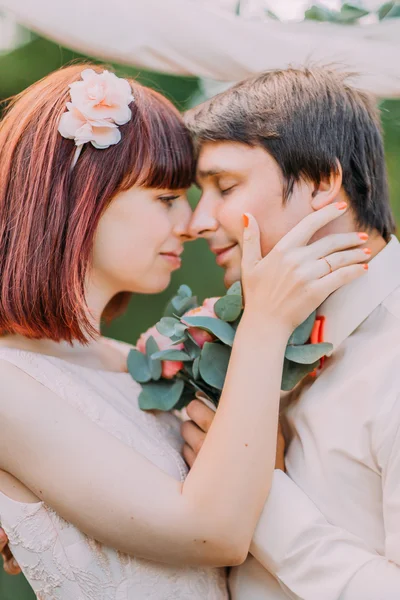 Encantadora novia en guirnalda mira con amor en el novio tocándose la nariz — Foto de Stock