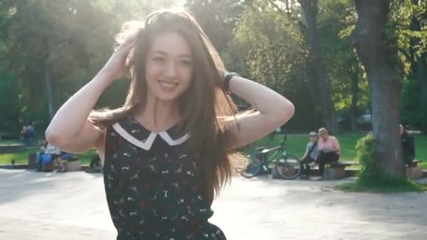 Молодая стильная брюнетка гуляет по зеленой аллее в парке и улыбается — стоковое видео