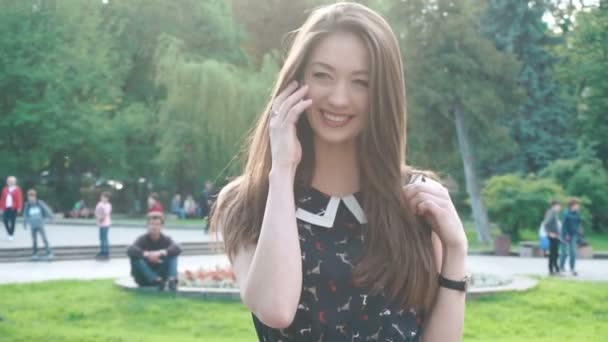 年轻时尚时髦女孩通话中绿色的春天公园和微笑 — 图库视频影像