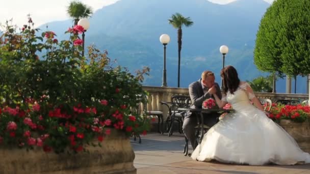 Bräutigam küsst Bräute im Sommercafé Hand in Hand. Flitterwochen auf der Insel Como, Italien — Stockvideo