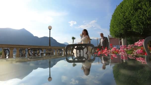 Ευτυχισμένη νύφη και τον γαμπρό με τα πόδια και κρατήστε τα χέρια στην πάρκο καλοκαιρινή βεράντα. Κόμο, Ιταλία — Αρχείο Βίντεο