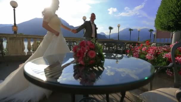 Los novios felices caminan y se toman de la mano en la terraza de verano. Lago de Como, Italia — Vídeo de stock