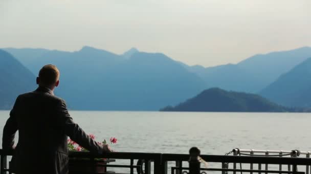 Sziluettjét jóképű vőlegény figyeli a hegyekre és a tóra néző, Como, Olaszország. Hátulnézet — Stock videók