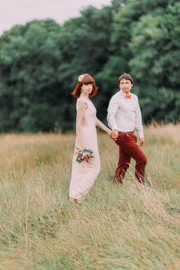 Gelin ve damat, düğün günü yürüyüş holding eller açık havada yaz doğa üzerinde