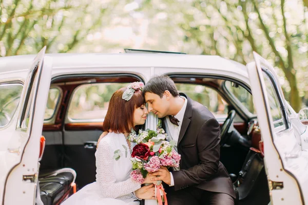 Prachtige kersverse bruid en bruidegom poseren achter hun trouwdag in retro auto — Stockfoto