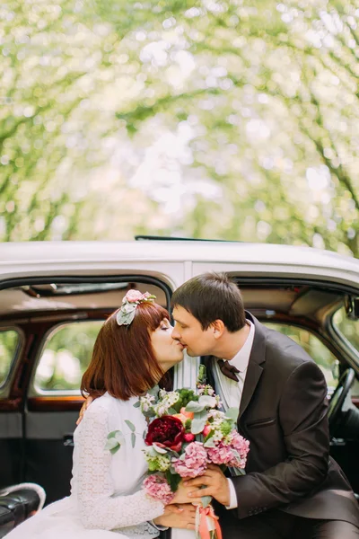 Novio guapo besa a su hermosa novia llegar a ella desde el asiento trasero de un coche — Foto de Stock