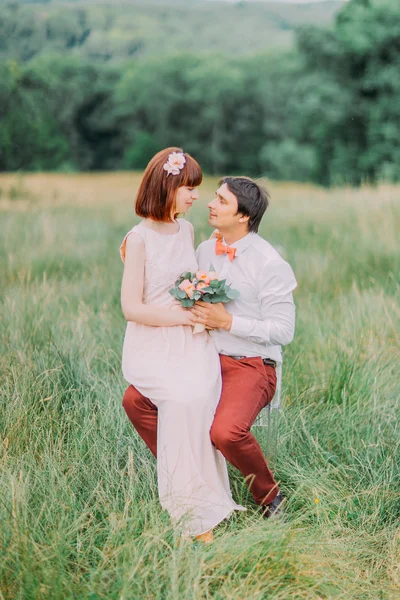 Schöne Braut sitzt auf den Beinen des Bräutigams im Park und schaut ihm in die Augen — Stockfoto