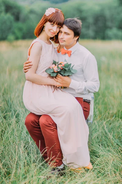 Красива наречена в чудовій сукні сидить на колінах наречених і обіймає його — стокове фото