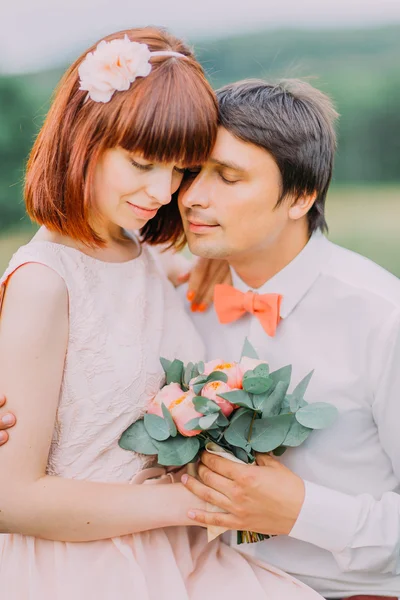 Bruidegom opent knuffels voor een schattige rode-hoofd bruid met boeket welke zittend op zijn knieën — Stockfoto