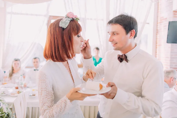 Primo piano dello sposo sorridente che alimenta la sua sposa con una torta nuziale, all'interno — Foto Stock