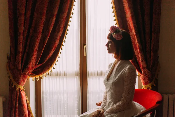 Calma novia sentada cerca de la ventana en el dormitorio, la mujer tiene la preparación final para la boda, el novio de espera . — Foto de Stock