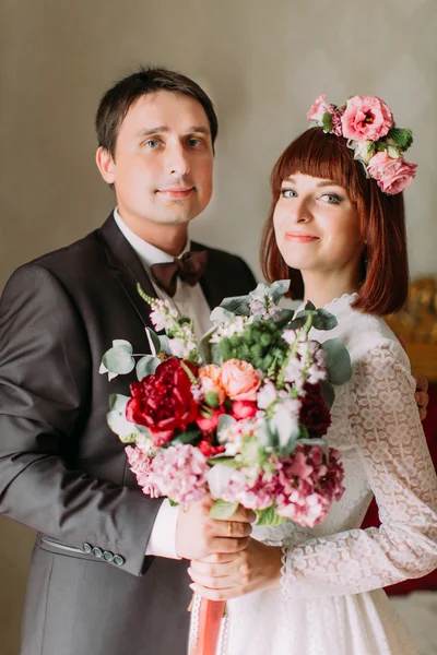 Groom embrassant sa mariée, tenant un bouquet dans une belle pièce éclairée — Photo