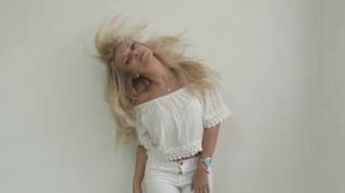 Beyaz üst çekici sarışın kız gülüyor ve beyaz düz duvar önünde saçları ile oynar