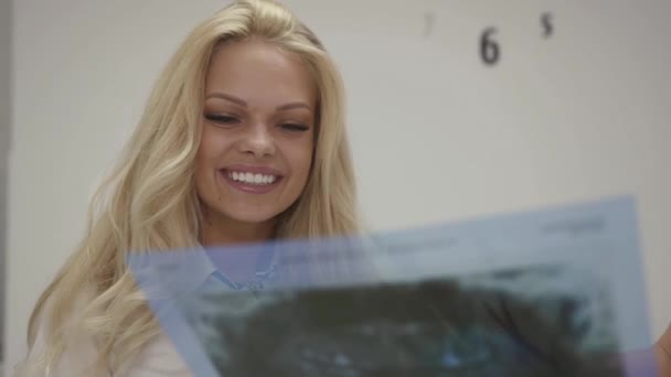 Schöne blonde Mädchen hört Oralspezialist mit ihr reden, hält Röntgenbild — Stockvideo