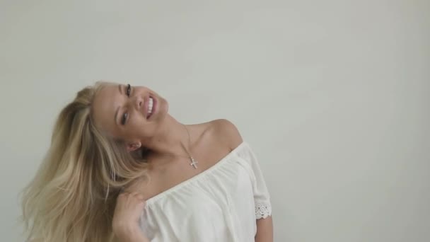 Nahaufnahmen aus dem Studio zeigen ein attraktives blondes Mädchen in weißem Top, das mit ihren Haaren spielt und lacht — Stockvideo