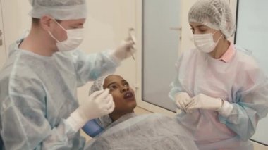 Scrup Kupası diş kliniğinde tıbbi prosedürler Bayan hasta Yapım Yardımcısı giyen dişçiyle yan görünüm resmi