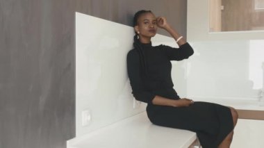 Masada oturan siyah giyinmiş ciddi Afro-Amerikalı kadın duvara yaslandı