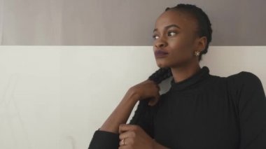 Koyu elbiseli güzel ve seksi siyah kadın stüdyoda gri duvara yaslanmış bakarak poz