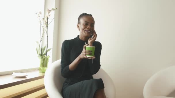 Primer plano de una joven sentada en silla blanca con café y teléfono móvil — Vídeos de Stock