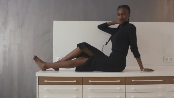 Side view of a serious african or black american woman sitting on desk and looking at camera — Stock Video