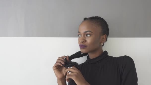 Okouzlující mladá Africká žena, která se dotýká dlouhých vlasů na pozadí studia — Stock video