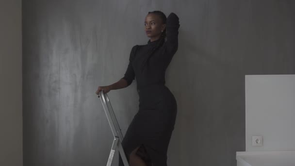 Close up portrait of beautiful young woman in black dress with hands over head, gray background — Stock Video