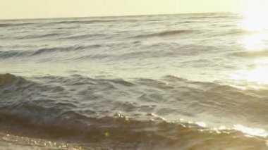 Deniz dalgaları gün batımında kum sahilde yuvarlanır. Rahatlatıcı sörf görüntüsü